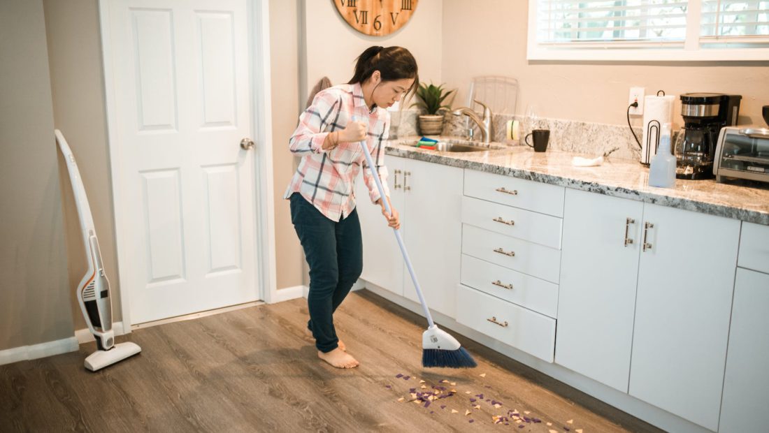 Photograph of a Woman in a Plaid Shirt Sweeping with a White Broom